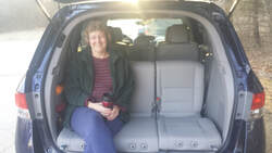 Peg Oberbeck seated in the back of her van's trunk, with the trunk door up. 